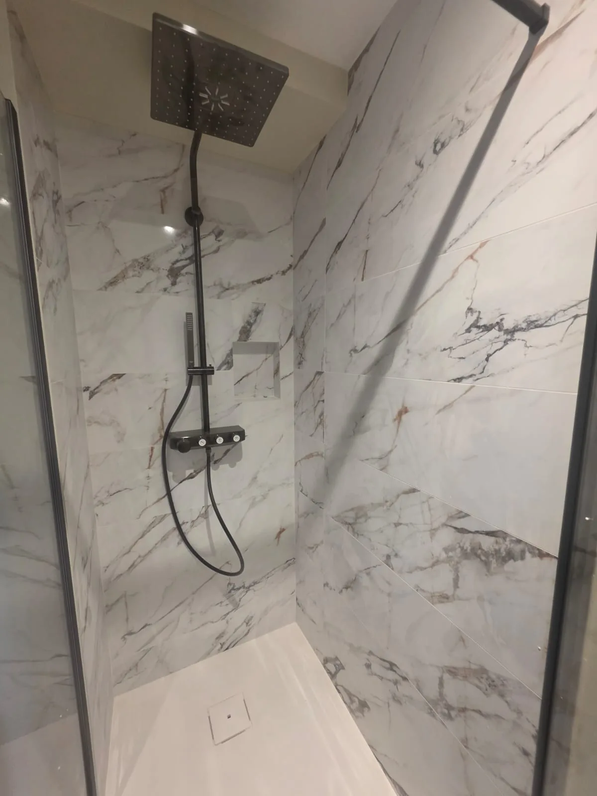Douche italienne en marbre blanc avec robinetterie noire, réalisée par AS de Bâtiment